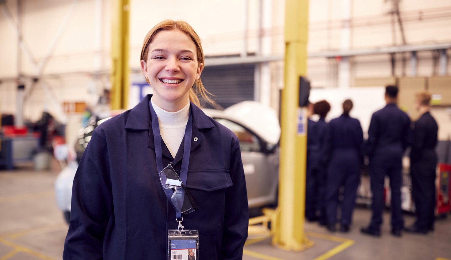 Female student standing in mechanic shop smiling