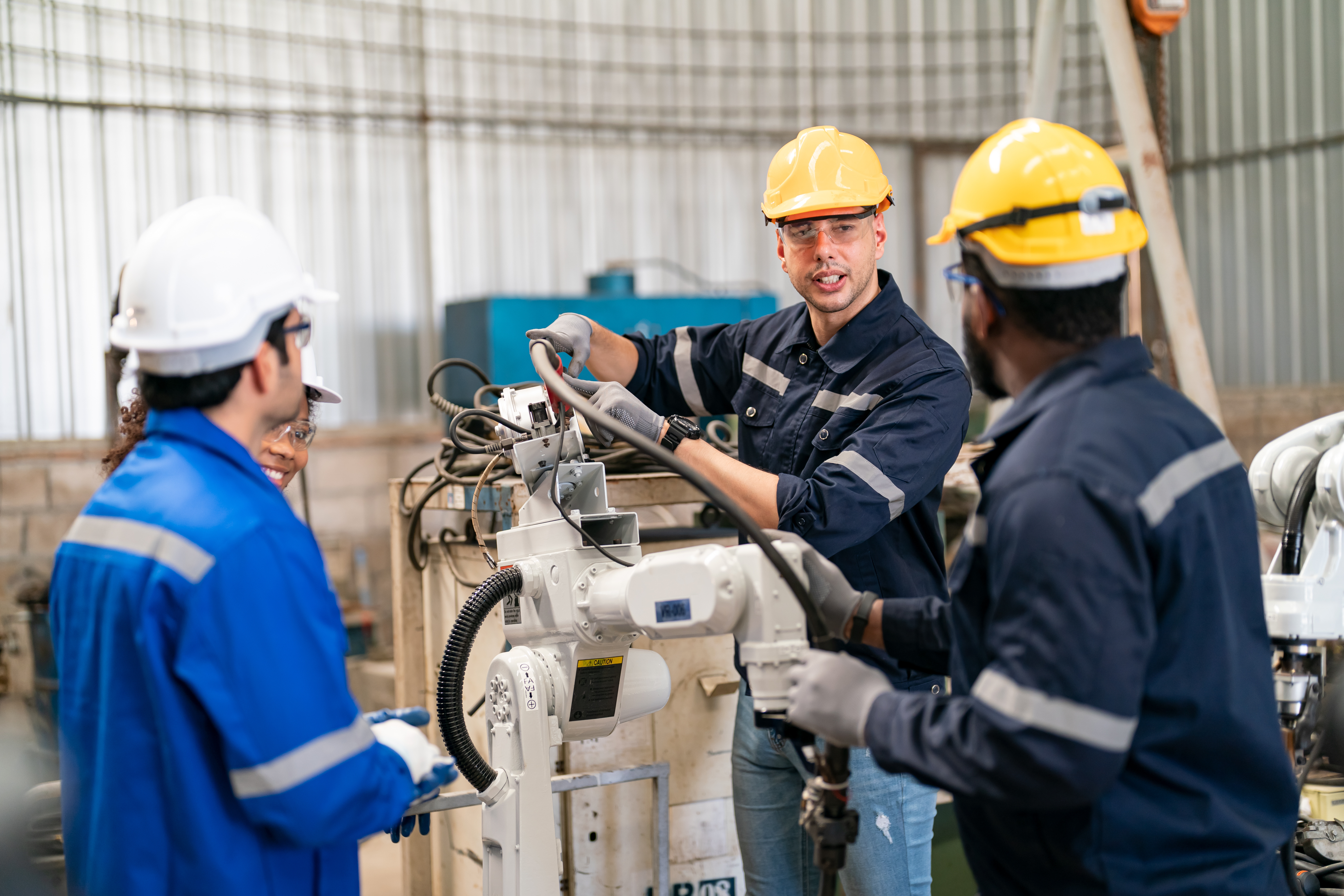 Three workers in a factory setting, wearing safety helmets and protective gear, collaborating on operating or repairing a large industrial machine.