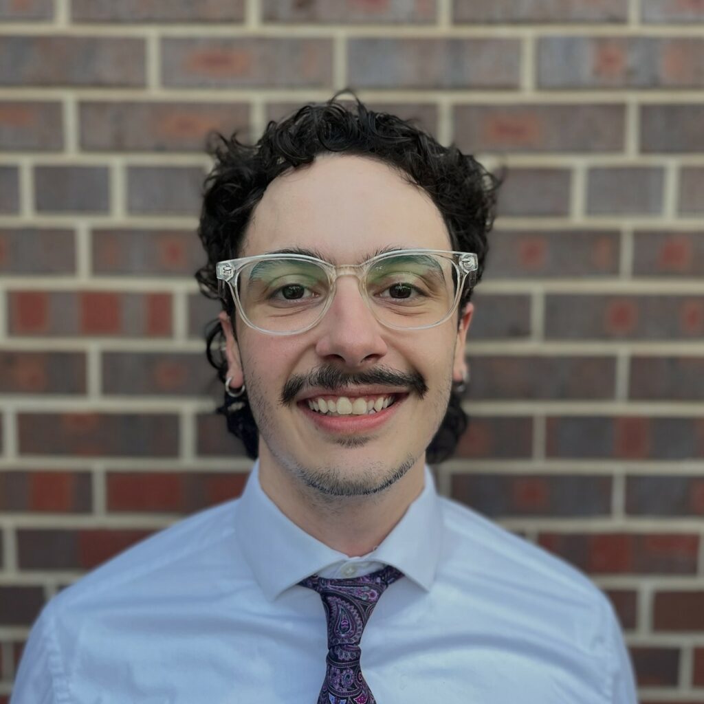 Dante LoCicero smiling in front of a brick background. 